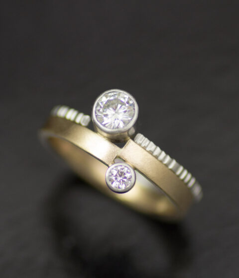 vis a vis bezel set moissanites in platinum and 14K yellow gold asymmetrical engagement ring with textured wedding band